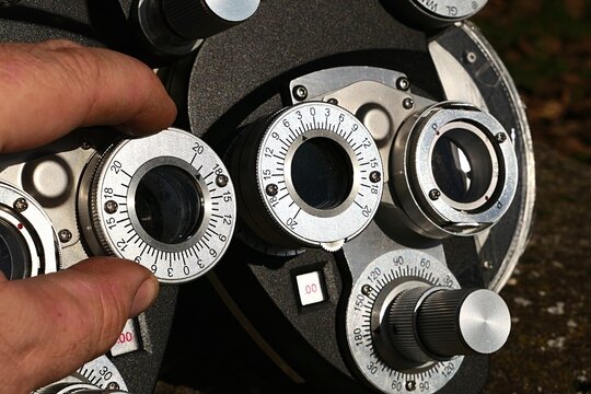 Detail of vintage manual mechanical phoropter, device used to determine patient refractive errors, hand of optometrist adjusting spherical values on left eye. Sunlit by autumn afternoon sunshine. 