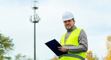 Male engineer in a helmet and overalls, an employee of a telecommunications company, inspects the...