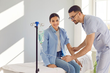 Young friendly male nurse help woman in receiving IV drip infusion or vitamin therapy in hospital....