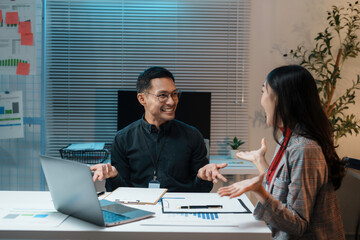 Asian business people celebrating success, discussing work and having fun together working late at night in modern office