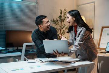 Obraz premium Excited business partners looking at laptop screen, celebrating business success and achievement working late in office at night