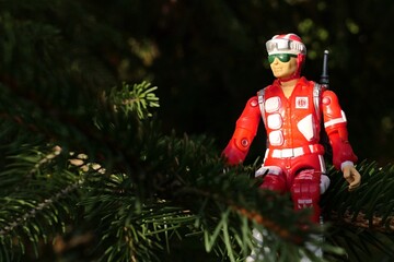 GI JOE action figure of military medic and rescue team member Lifeline, version from 1986, sitting on a branch of spruce tree, sunlit by bright autumn sunshine, looking like christmas tree decoration.