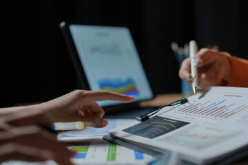 Business partners are working late analyzing financial charts and graphs using a digital tablet for research