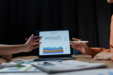 Two businesswomen are analyzing a financial report on a digital tablet during a night meeting
