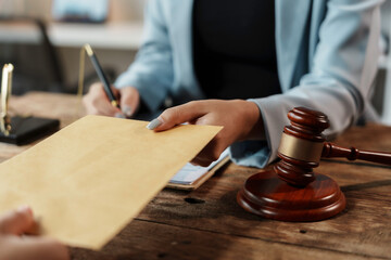 Lawyer is giving an envelope to a client over a wooden desk with a gavel on it