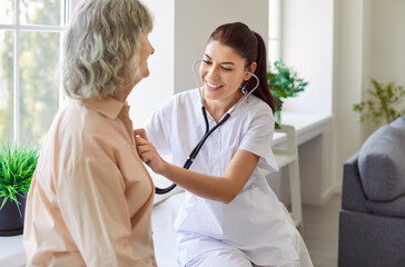 Positive female doctor or nurse uses a stethoscope to listen to the lungs of an elderly patient...