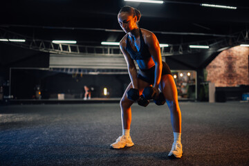 Obraz premium Young athletic woman lifting heavy dumbbells in a gym