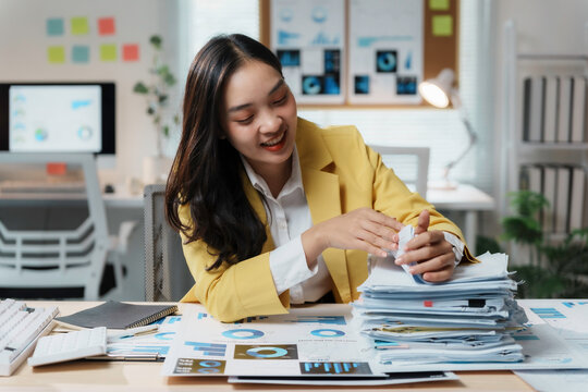 Asian businesswoman is smiling while organizing a stack of documents at her desk in an office