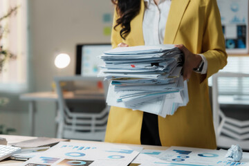 Stressed businesswoman in a busy office with a huge stack of paperwork, showing the challenges of...