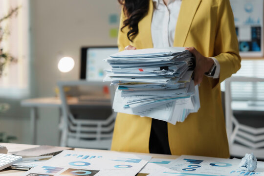 Stressed businesswoman in a busy office with a huge stack of paperwork, showing the challenges of managing documents in a corporate setting