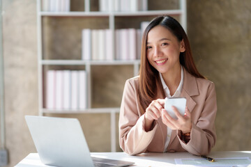 Fototapeta premium Confident asian businesswoman happily uses her smartphone in a modern office, balancing work and technology in a stylish workspace