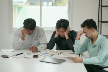 Three businessmen are feeling stressed while working together in the office with documents spread out on the table