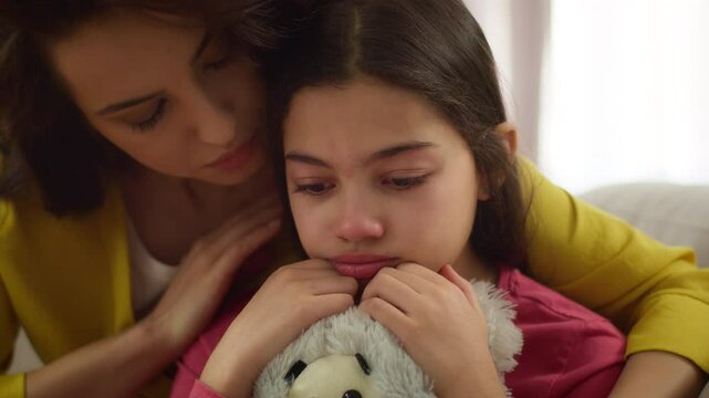 Caring Caucasian worried woman babysitter sister female mother comforting calming stroking crying upset little girl child adopted sad kid daughter cry hug toy bear indoor home. Bullying trauma stress