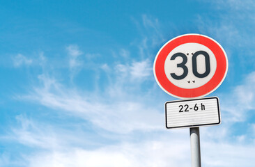 Speed limit sign indicating 30 km/h with time restrictions under a bright blue sky