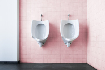 Front view of the interior of a public bathroom with two urinals for men. The decoration is clean...