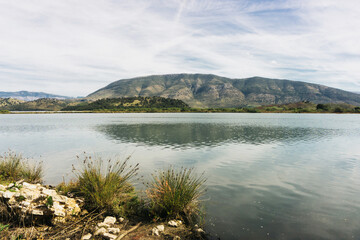 Mountain lake with blue sky. Clear water landscape. Calm lake surface with mountains on the horizon. Beautiful nature background with summer vibes. Holiday in Albania. Vacation trip to Butrint.
