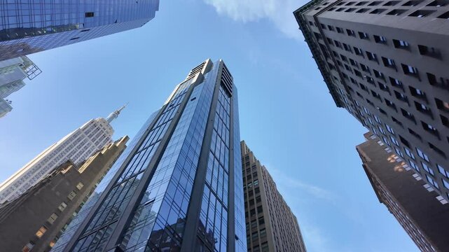 A low angle view of the tall skyscrapers in midtown Manhattan on a clear blue sky sunny day.  	