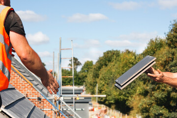 Construction workers collaborate on a sunny day, passing tiles for roof installation at a bustling building site