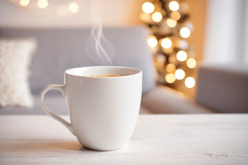 Cozy scene with steaming white cup of coffee on light wooden table, with blurred festive background of warm golden bokeh lights. For themes of relaxation, holidays, warmth, and cozy home atmospheres