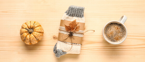 Warm socks with cup of coffee and pumpkin on beige wooden background