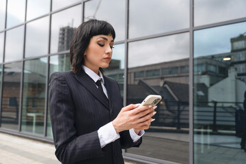 Business professional checks smartphone outside modern office building on a cloudy day