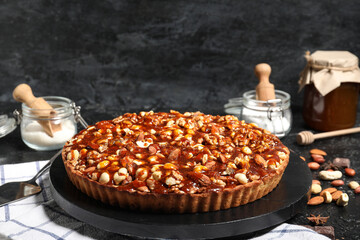 Board of sweet tart with different nuts and caramel on black background