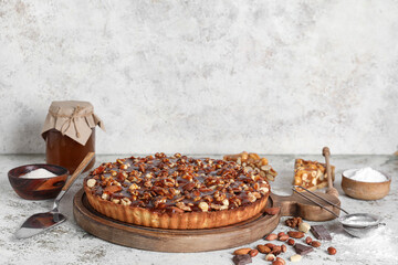 Wooden board of sweet tart with different nuts and ingredients on white background
