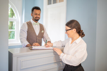 A receptionist is helping a guest with check-in at a stylish hotel lobby. The warm atmosphere and attentive service create a welcoming experience for visitors.