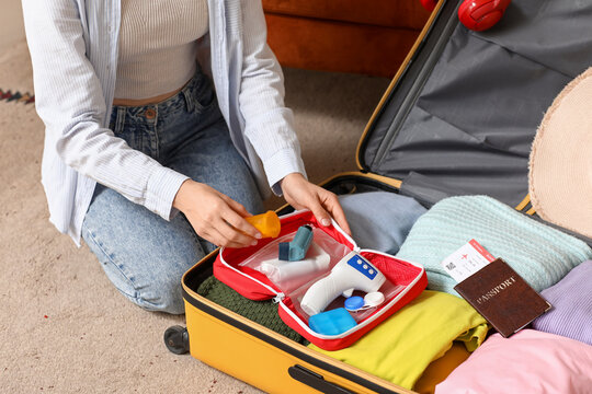 Young woman with suitcase packing first aid kit on floor at home, closeup. Travel concept