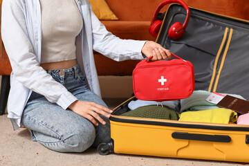 Young woman with suitcase and first aid kit sitting on floor at home, closeup. Travel concept