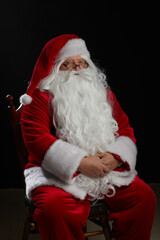 Santa Claus sits on a black background and looks at the camera. Christmas, New Year, Holiday Celebration