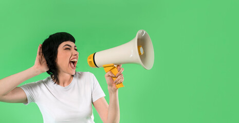 A young woman passionately delivers a message using a megaphone against a bright green backdrop