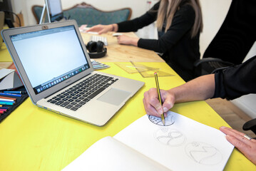 creative people from the company's marketing department work on defining a new product logo, drawing a sketch by hand and then refining it on the computer 