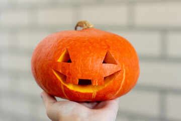 Funny carved Halloween pumpkin on hand on bricks background