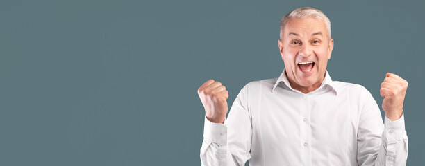 Yes. Excited senior man screaming with joy, raising clenched fists in the air isolated over blue...