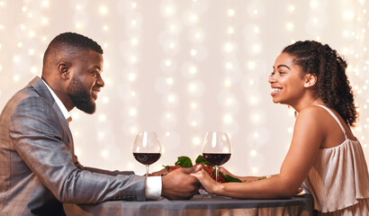 Romantic african american couple in love having date at restaurant, drinking red wine and holding hands, side view, empty space