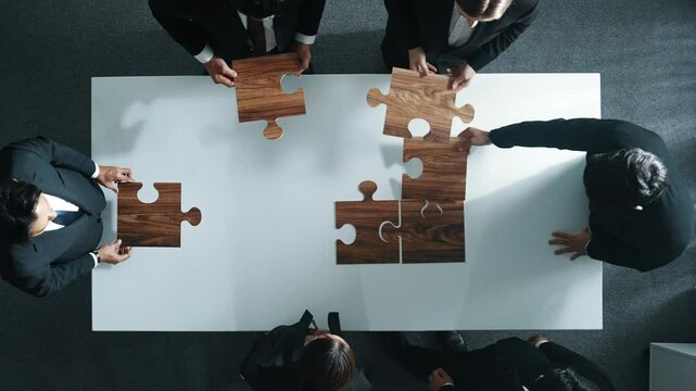 Top view of business people putting jigsaw together at meeting room. Professional marketing team standing at table while gathering puzzle piece. Show unity, cooperation and team working. Directorate.