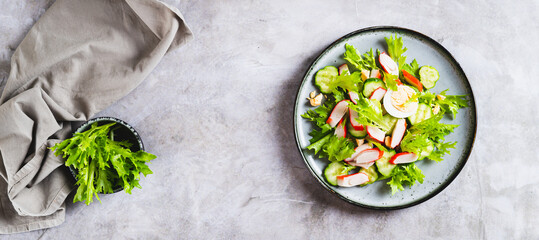 Appetizing salad of crab sticks, cucumber, leaves and egg on a plate top view web banner © elenarui