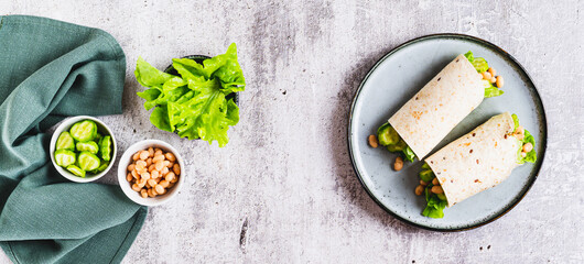 Beans, cucumber and leaves wrapped in tortilla roll on plate on table top view web banner