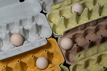A yellow, brown, white, and green egg carton filled with eggs and made from recycled paper. This...