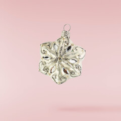 Christmas holliday image, Christmas bauble in shape of a snowlfake falling in the air isolated on pink background