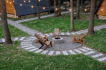 Cozy fire pit seating area in forest glamping with glowing string lights and modern wooden cabins