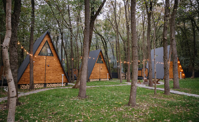 Cozy wooden A-frame cabins in forest with sunlight and outdoor seating area