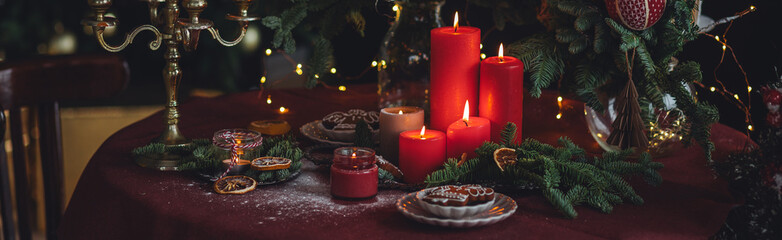 Christmas and New Year beautiful elegant family dinner table setting decorated with red candles, fir tree branches, homemade gingerbread cookies. Banner