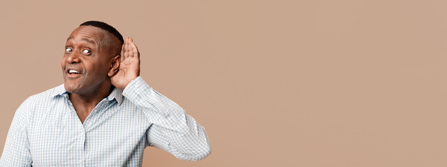 Curious interested mature african american man holding hand near ear and trying to hear...