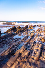 Beautiful sharp stones on the seashore, washed by the waves. Stone ridges on a wild beach. Smooth and long stone formations going into the sea. Beautiful photo of marine nature