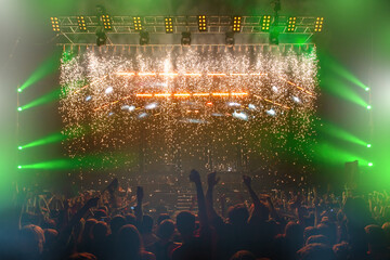 Concert stage in front of audience. Backs fans at night stadium. Bright light show at concert. Scene with beams spotlights and light music. Popular music festival with spectators. Rock band concert