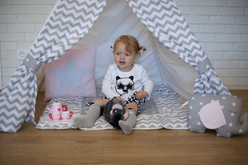 Adorable beautiful happy smiling ginger-haired toddler little girl is playing with her toys sitting in a teepee wigwam © Tina