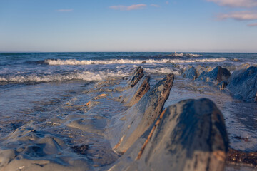 Beautiful sharp stones on the seashore, washed by the waves. Stone ridges on a wild beach. Smooth and long stone formations going into the sea. Beautiful photo of marine nature