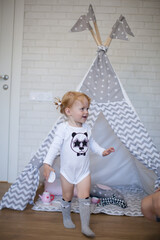 Adorable beautiful happy smiling ginger-haired toddler little girl is playing with her toys sitting in a teepee wigwam © Tina